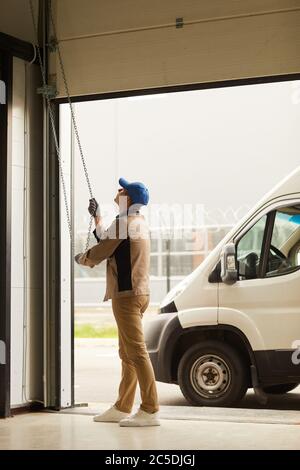 Manual worker in uniform opening the garage for the van he working in warehouse Stock Photo