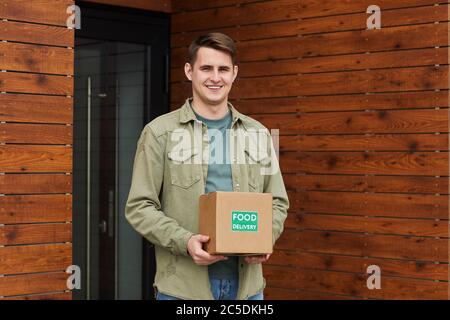 Portrait of young man getting parcel and smiling at camera while standing outdoors near the post office Stock Photo