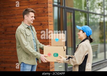 Young man getting his parcels from the courier while they standing outdoors Stock Photo
