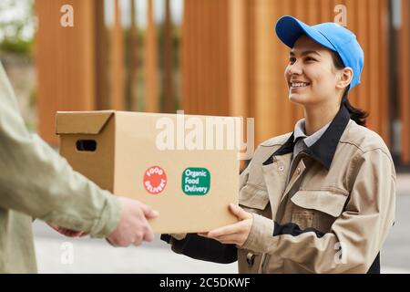 Young smiling courier in uniform delivering the parcel to man outdoors Stock Photo