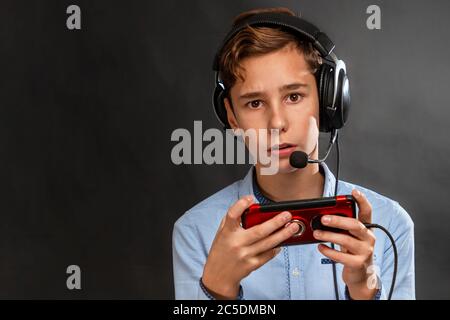 A teenager wearing headphones is playing a game on his smartphone. Copy space. Dark background. The concept of entertainment and modern technology. Stock Photo