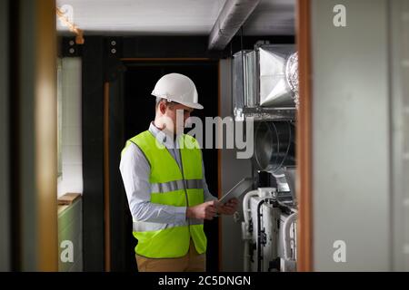 Young engineer in work helmet using digital tablet while working in the factory Stock Photo
