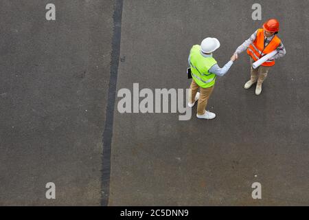 High angle view of two engineers in reflective vests and in work helmets shaking hands while they standing outdoors Stock Photo