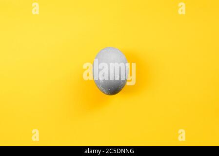 Gray colored easter egg on yellow background. Closeup of single boiled chicken egg dyed in color of concrete. Top view, flat lay. Happy Easter concept Stock Photo