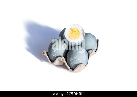 Four easter eggs in color of concrete in cardboard tray and one boiled egg is cut on white background. Happy Easter concept. Copy space Stock Photo