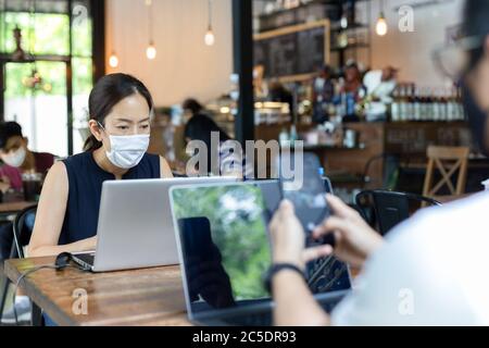 New normal woman wearing protective mask while working on laptop in cafe. Stock Photo