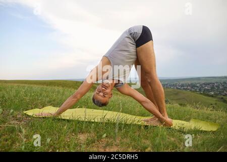 Yoga in nature. Male yogi posing practicing yoga meditation on the field on the nature in summer. Stock Photo