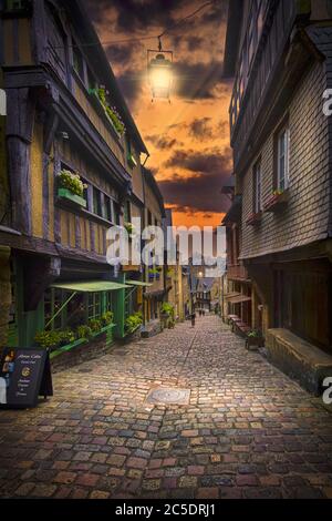 Rue du Jerzual, Dinan, Brittany, France. Sunset view of this old street illuminated by street lamps and lined with typical half-timbered buildings. Stock Photo