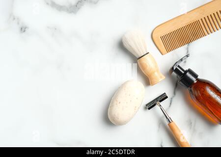 Shaving accessories for man on marble table. Flat lay composition with handmade soap, razor, shaving brush, bottle with foam gel, wooden hair comb. Stock Photo