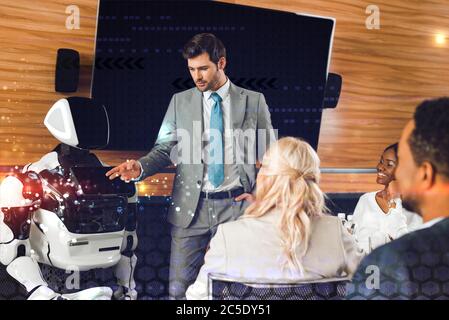 handsome businessman pointing with hand at robot near multicultural colleagues Stock Photo