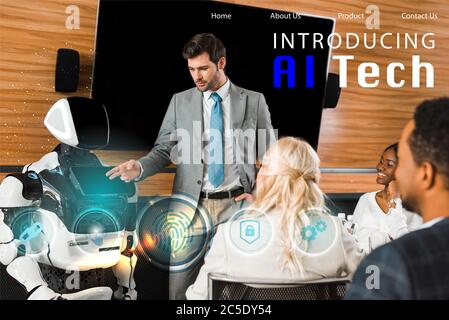 handsome businessman pointing with hand at robot near multicultural colleagues, ai tech illustration Stock Photo