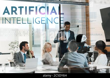 handsome african american businessman showing robot to multicultural colleagues in office, Artificial Intelligence illustration Stock Photo
