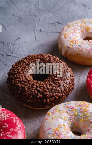 Chocolate, pink and vanilla donuts with sprinkles, sweet glazed dessert food on concrete textured background, angle view macro Stock Photo