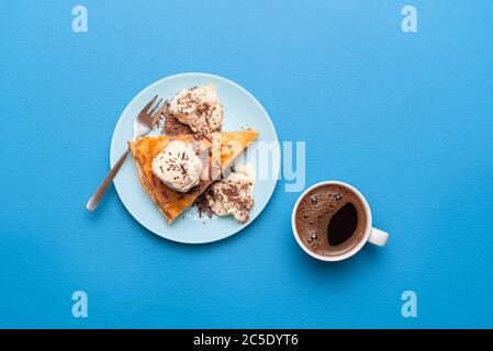Apple pie slice with golden crust served with vanilla ice cream and a hot coffee on a blue table. Flat lay with an apple tart. Thanksgiving dessert. Stock Photo