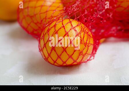 Satsuma oranges in red nylon packaging lying on white surface Stock Photo