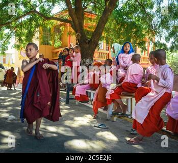 Amarapura, Mandalay, Myanmar - Young Buddhist monks at school in monastery. Boys wearing dark red robe and girls wearing pink robe. Stock Photo