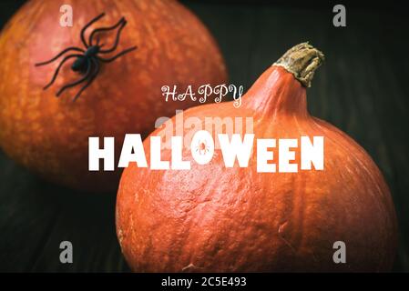 Happy Halloween banner. Pumpkins and black spider on dark table. Halloween typography on food background. Natural pumpkins on vintage wooden boards cl Stock Photo