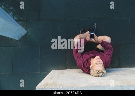 Caucasian young man in sportswear sitting on the ground, resting after training and listening to music on headphones Stock Photo