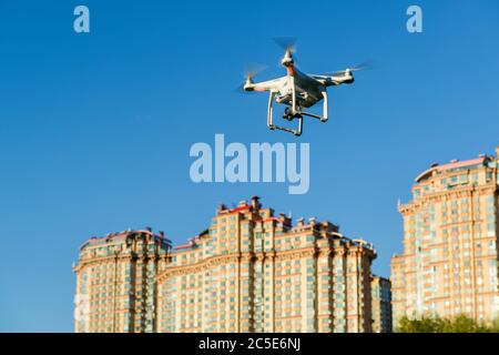 Drone quad copter with onboard high resolution digital camera flying over the city in the blue sky Stock Photo