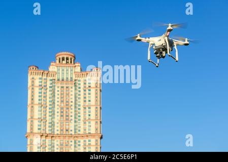 Drone quad copter with onboard high resolution digital camera flying over the city in the blue sky. Stock Photo