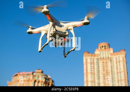 Drone quad copter with onboard high resolution digital camera flying over the city skyscrapers in the blue sky Stock Photo