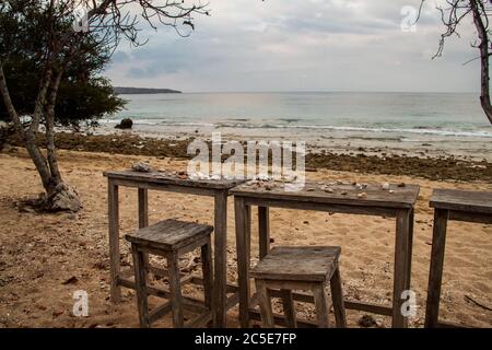 A wide angle image of a wooden table and chairs with sheshells on it at the beach Stock Photo