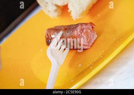Grilled sausage on a fork and bread on a yellow plastic plate. Disposable tableware Stock Photo