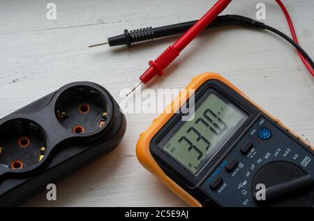 Multimeter and electric splitter on a white wooden background. Measurement of electric network parameters. Electrical safety. Qualified electrician se Stock Photo