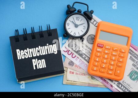 RESTRUCTURING PLAN text with alarm clock, banknotes currencies, notepad and calculator on blue background. Coronavirus Covid19 and Business Concept Stock Photo