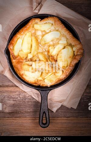 Apple Tarte Tatin, in cast iron skillet resting, on baking parchment over old wood background. Retro style processing with intentional vignette. Stock Photo