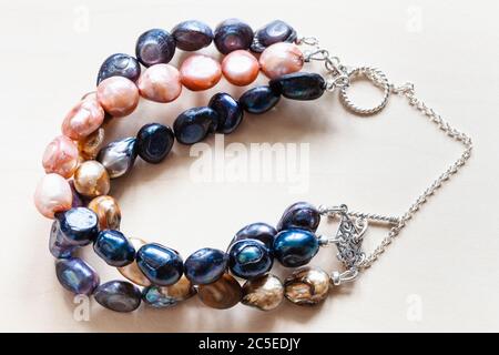 handmade bracelet from three stings of dyed natural river pearls and silver chain and clasp closeup on pale wooden table Stock Photo