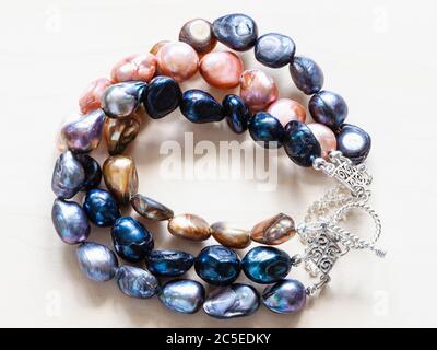handcrafted bracelet from three stings of colored natural river pearls and silver chain and clasp closeup on pale wooden board Stock Photo