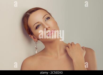 The brunette woman in beautiful earrings, looking up daydreaming isolated on a light gray background. Multicultural ethnic mixed race hispanic latin c Stock Photo