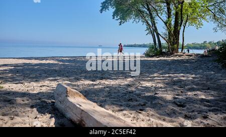 Young couple take a walk on an isolated area of a wide sandy beach during sunny summer day on shores of Lake Ontario near the Welland Canal. June 2020. Stock Photo