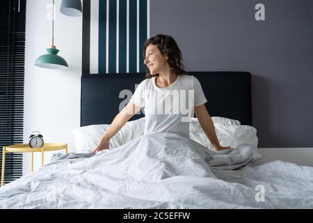 Beautiful girl wakes up in a good mood in a stylish apartment. Stretches with a smile starting the day. Stock Photo