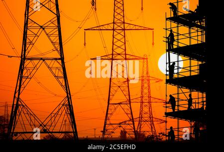 Construction/building workers on scaffolding with electricity pylons at sunrise overlayed, UK. Concept image: building industry, energy, employment. Stock Photo