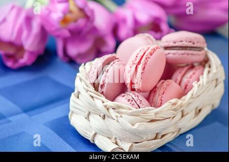 traditional French multicolored macaroons rows in a basket on the background of a bouquet of flowers. Close-up, selective focus. Stock Photo