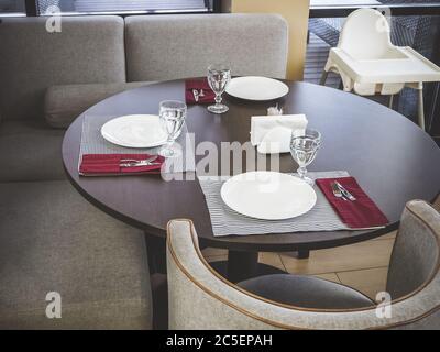 On a round table are cutlery for three people, next to a soft gray sofa and armchair Stock Photo