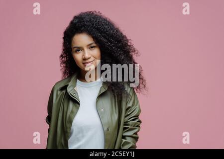 Isolated shot of serious dark skinned woman looks with confident calm expression at camera, listens something very attentively, dressed in stylish out Stock Photo