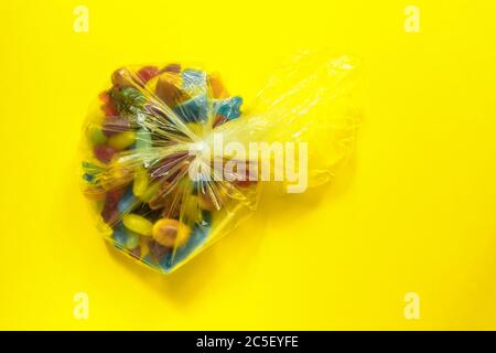 Multi-colored glazed jelly beans sweets in plastic package on yellow paper background. Stock Photo