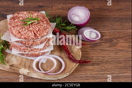 Raw burger cutlets made from minced fresh meet with spices and herbs on wooden background. Ingredients for making burgers. Stock Photo