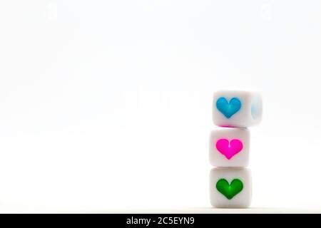 Three colorful heart symbols piled on white cubes isolated on white background, pink, blue and green Stock Photo