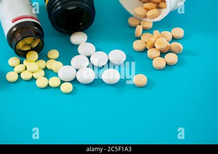 Orange, yellow and white pills and bottles for pills on a blue background. Pills scattered with white and glass jars. Stock Photo