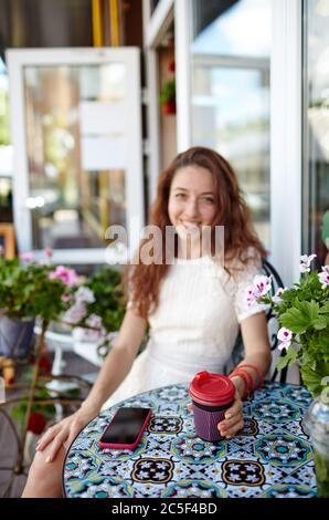 Beautiful attractive woman drinks cofee in the cafe. Coffee break. Smart phone on the table. Focus on hands Stock Photo