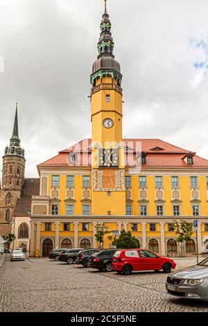 Bautzen's town hall (Sorbian: Radnica) rises with its Baroque tower above the main square in Bautzen, Saxony, Germany. A clock face and an ornate sundial decorate the tower's south side. To the left stands the pointed spire of St. Petri Cathedral. The tower's foundation stone dates from 1489, and its first clock was added in 1525. The town hall itself received its present Baroque form between 1729 and 1732. Stock Photo
