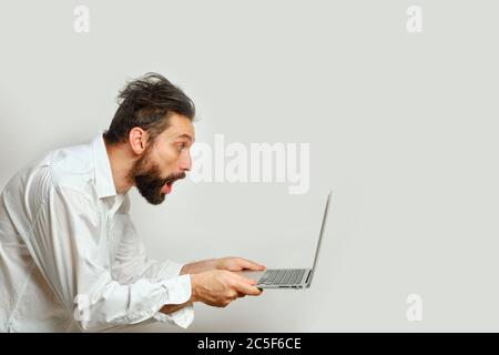 Young Caucasian man looks in surprise at a laptop monitor Isolated on a white background. Human emotions, facial expression concept Stock Photo