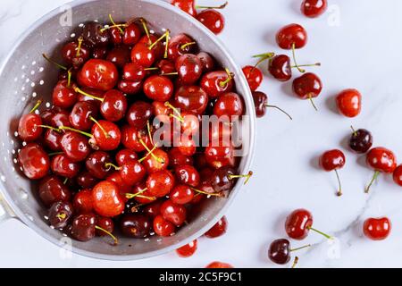 Berry cherries in colander bowl with water drops on white background. Top view. Stock Photo