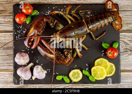 Uncooked fresh lobster on black board with spices and vegetables. Top view. Stock Photo