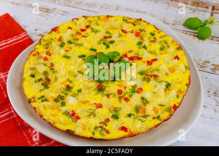 Homemade omelette with vegetables on white plate on wooden background. Stock Photo