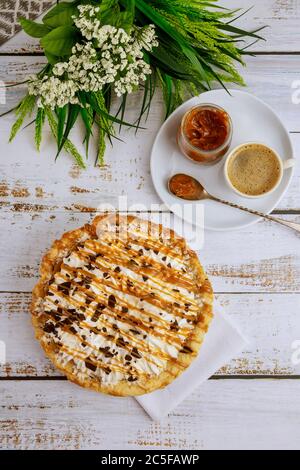 Party cake with caramel sauce, chocolate and coffee on white background with flowers. Top view. Stock Photo